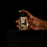 Hand holding a bottle of 'Alpha Gold Men' cologne against a black background