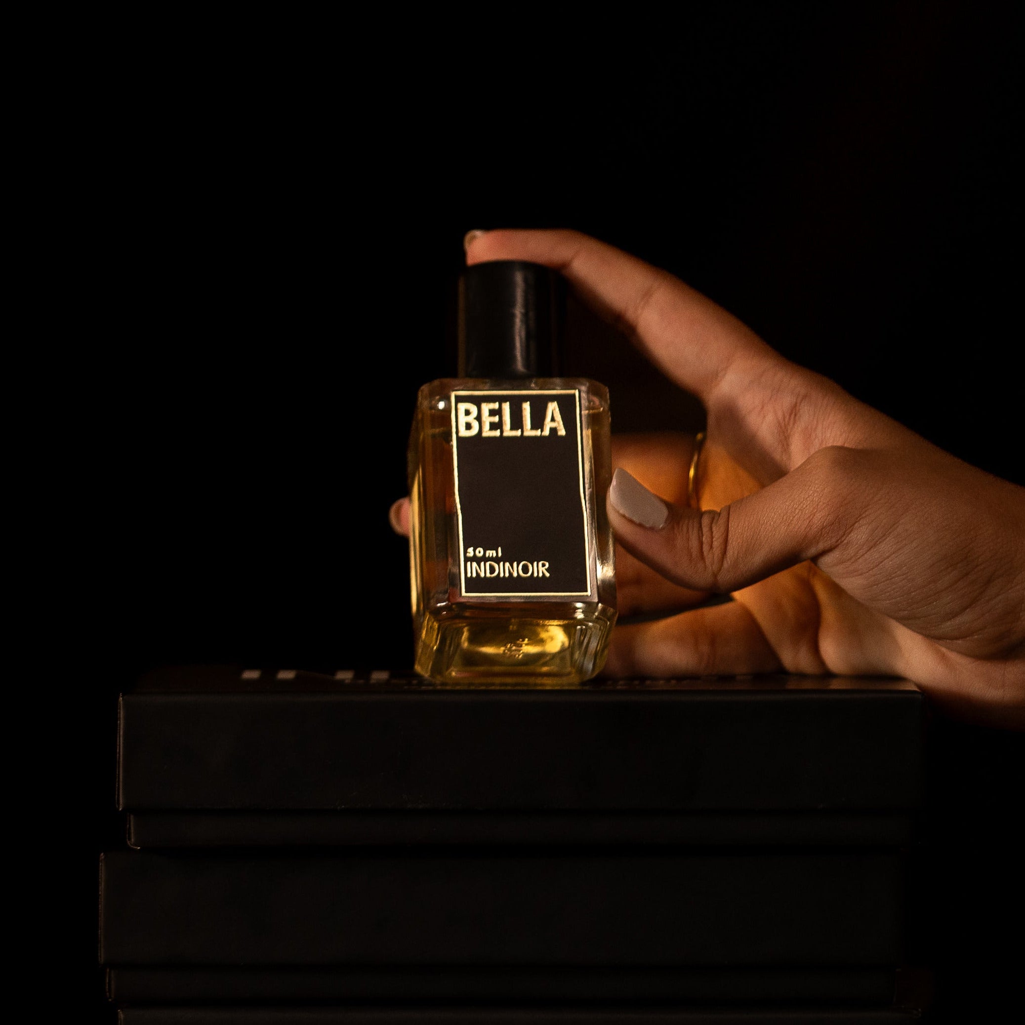 Hand holding a bottle labeled 'BELLA' on a black background