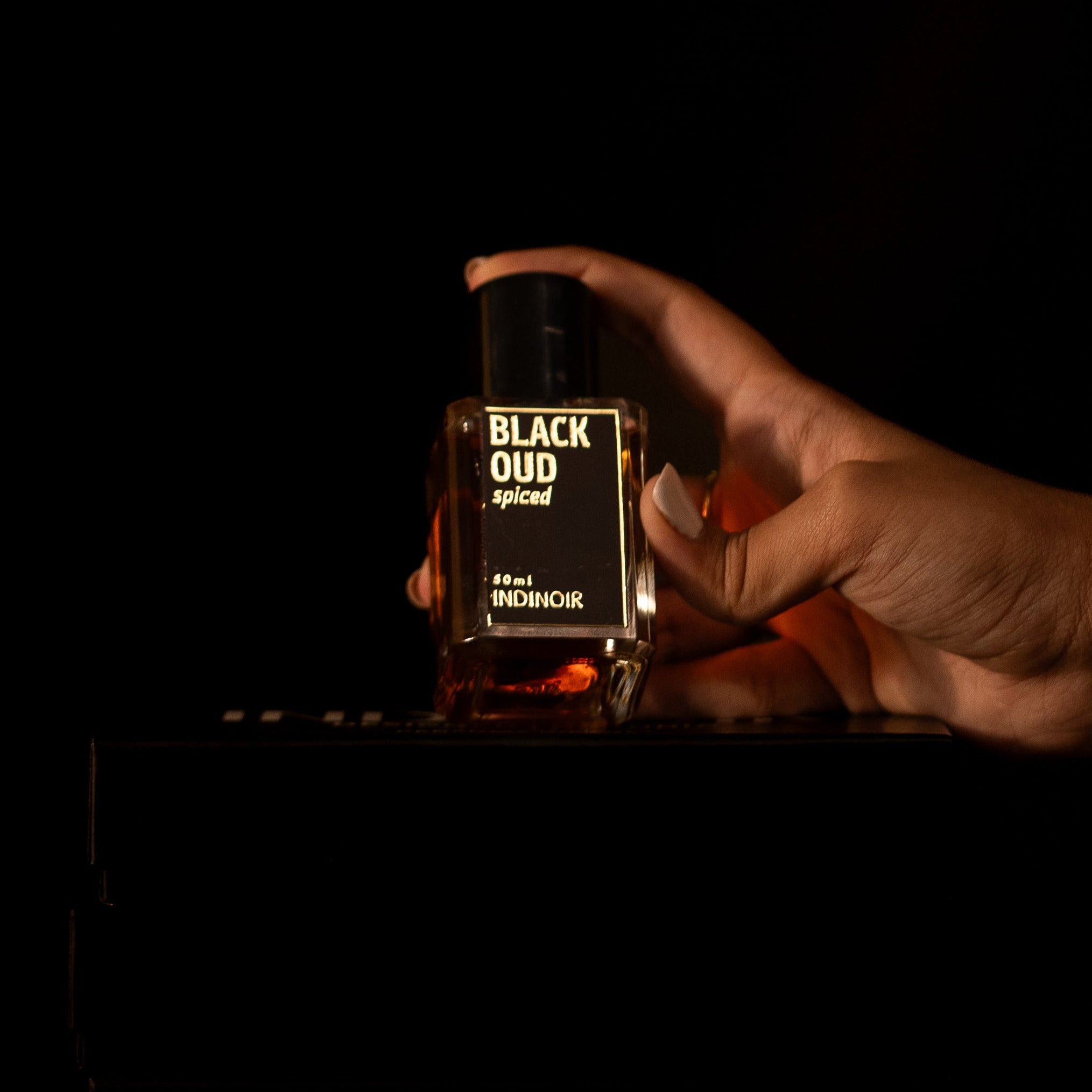 Hand holding a perfume bottle labeled 'Black Oud' against a dark background