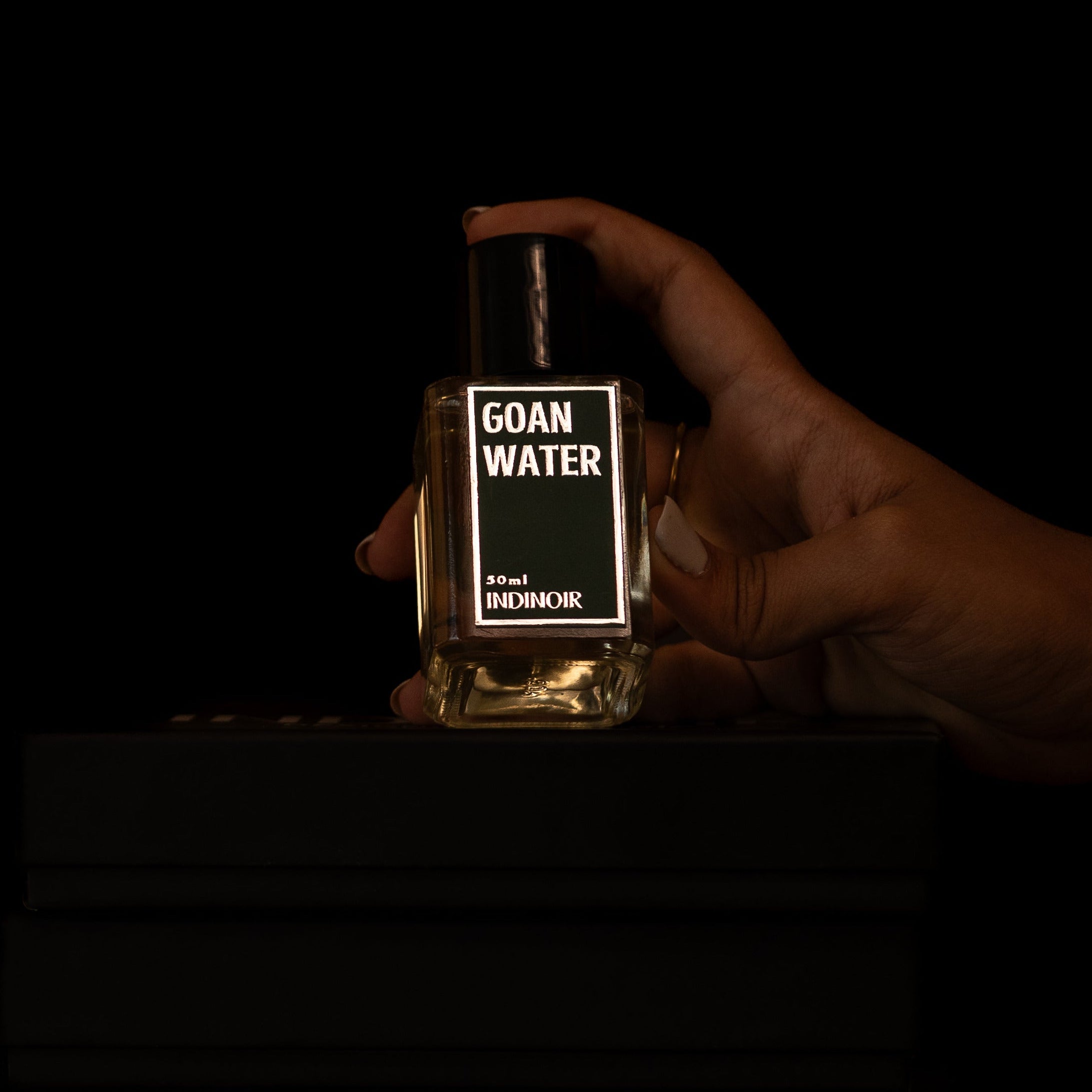 Hand holding a bottle labeled 'GOAN WATER' against a dark background
