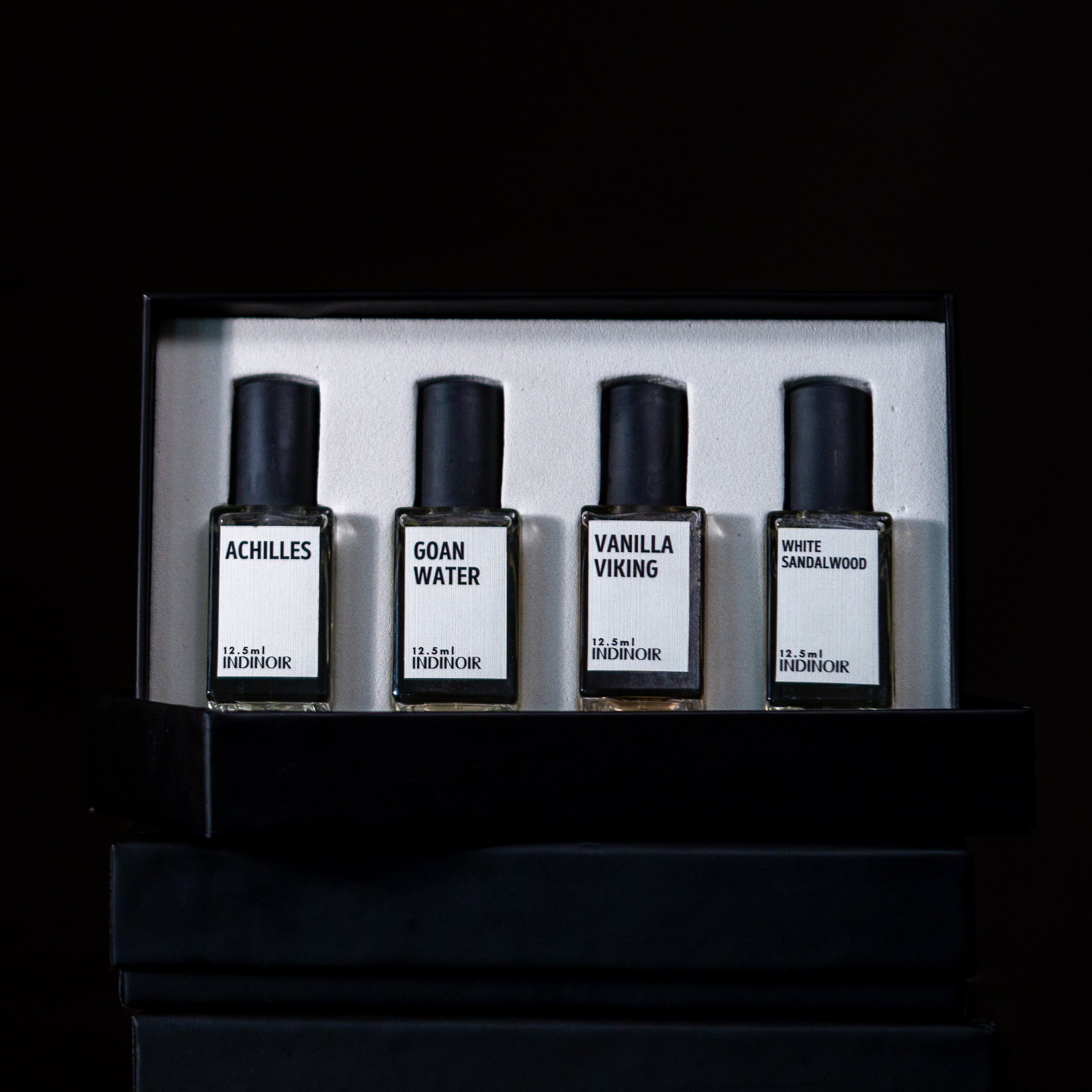 Set of four perfume bottles in a display case on a dark background