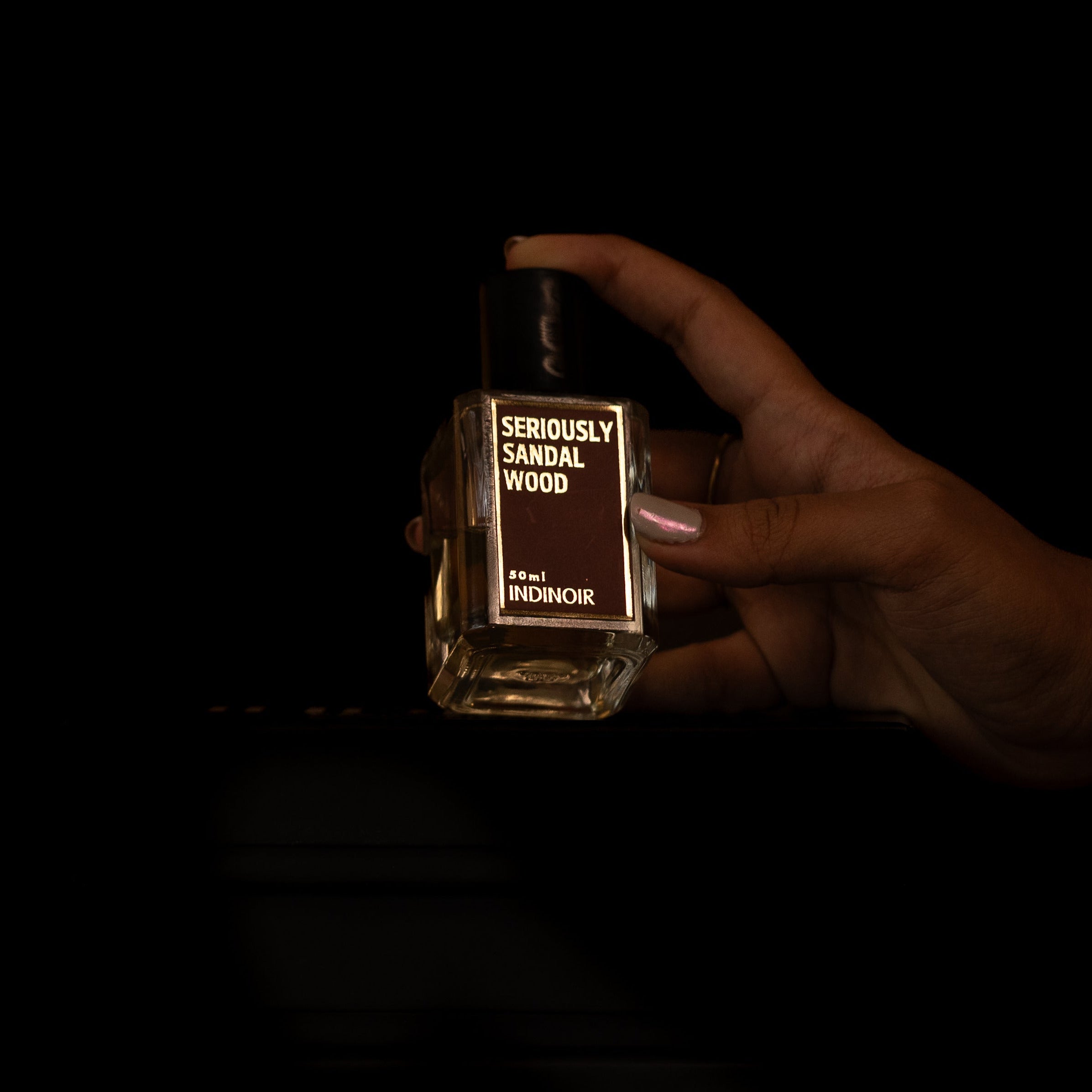 Hand holding a bottle of 'Seriously Sandalwood' cologne against a dark background