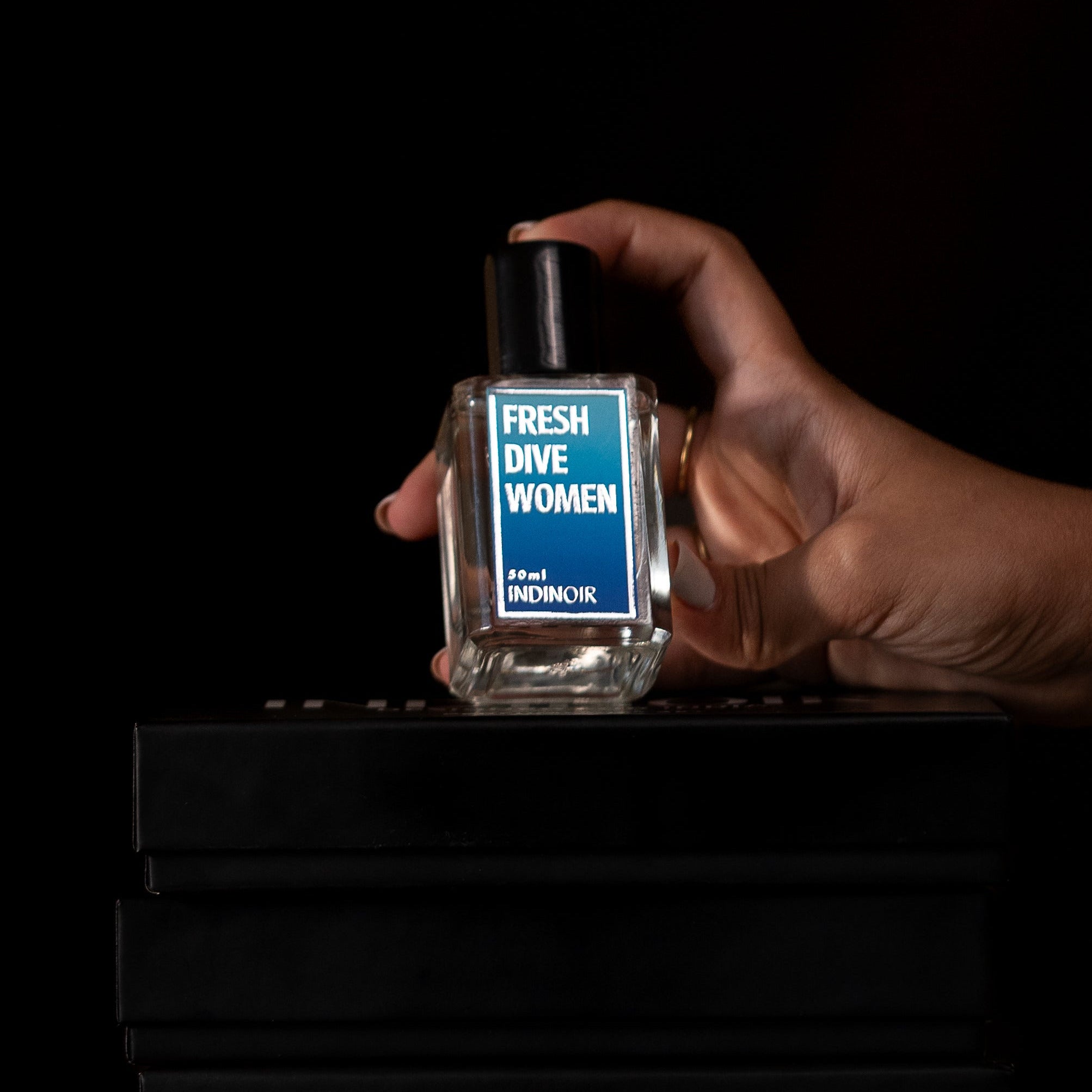 Hand holding a perfume bottle labeled 'Fresh for Women' on a black background