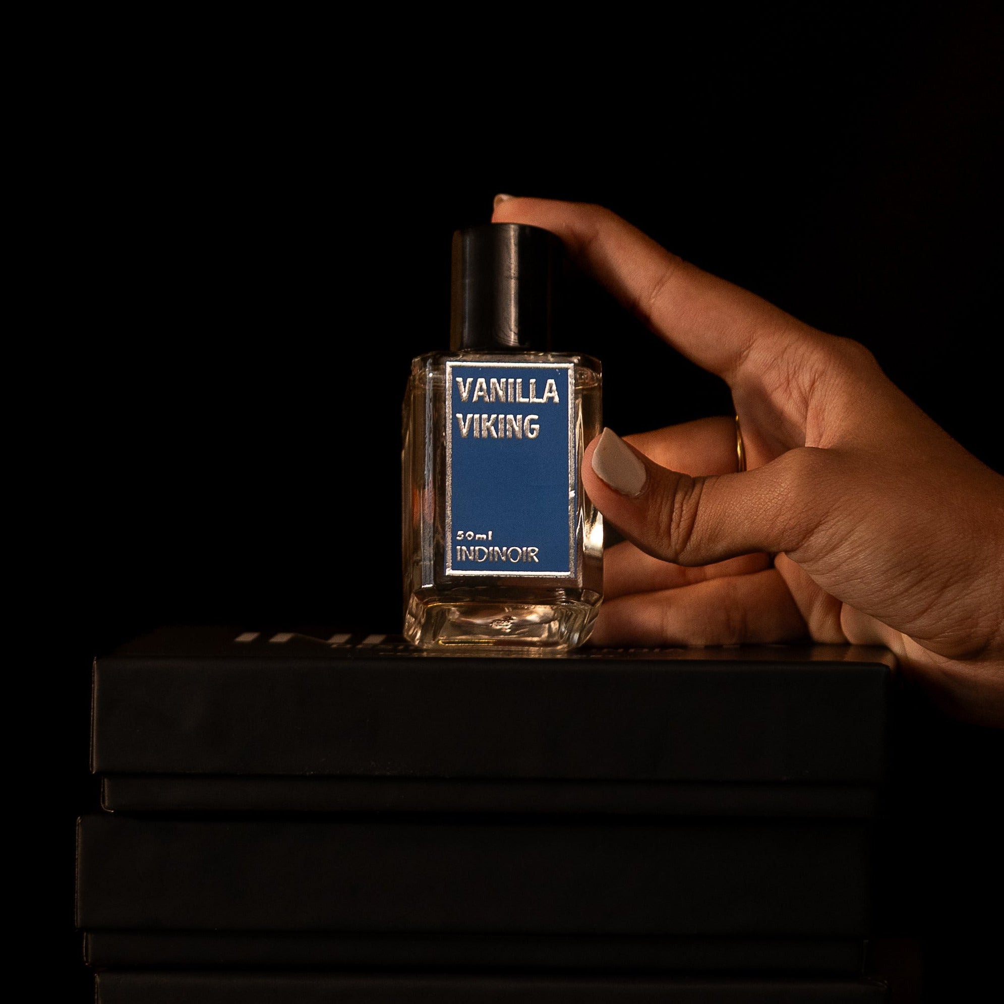 Hand holding a small bottle labeled 'Vanilla Viking' against a black background