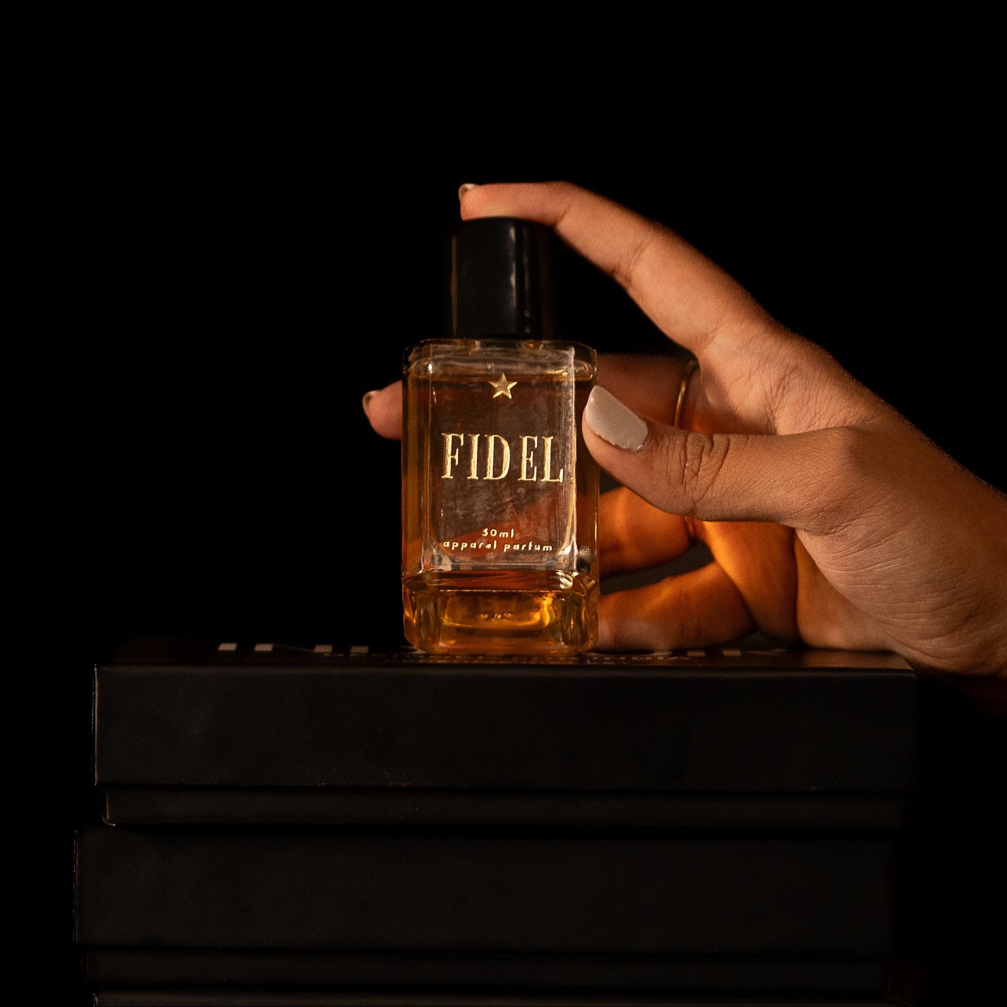 Hand holding a bottle labeled 'FIDEL' on black boxes with a dark background